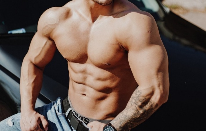 topless man in blue denim jeans sitting on car hood